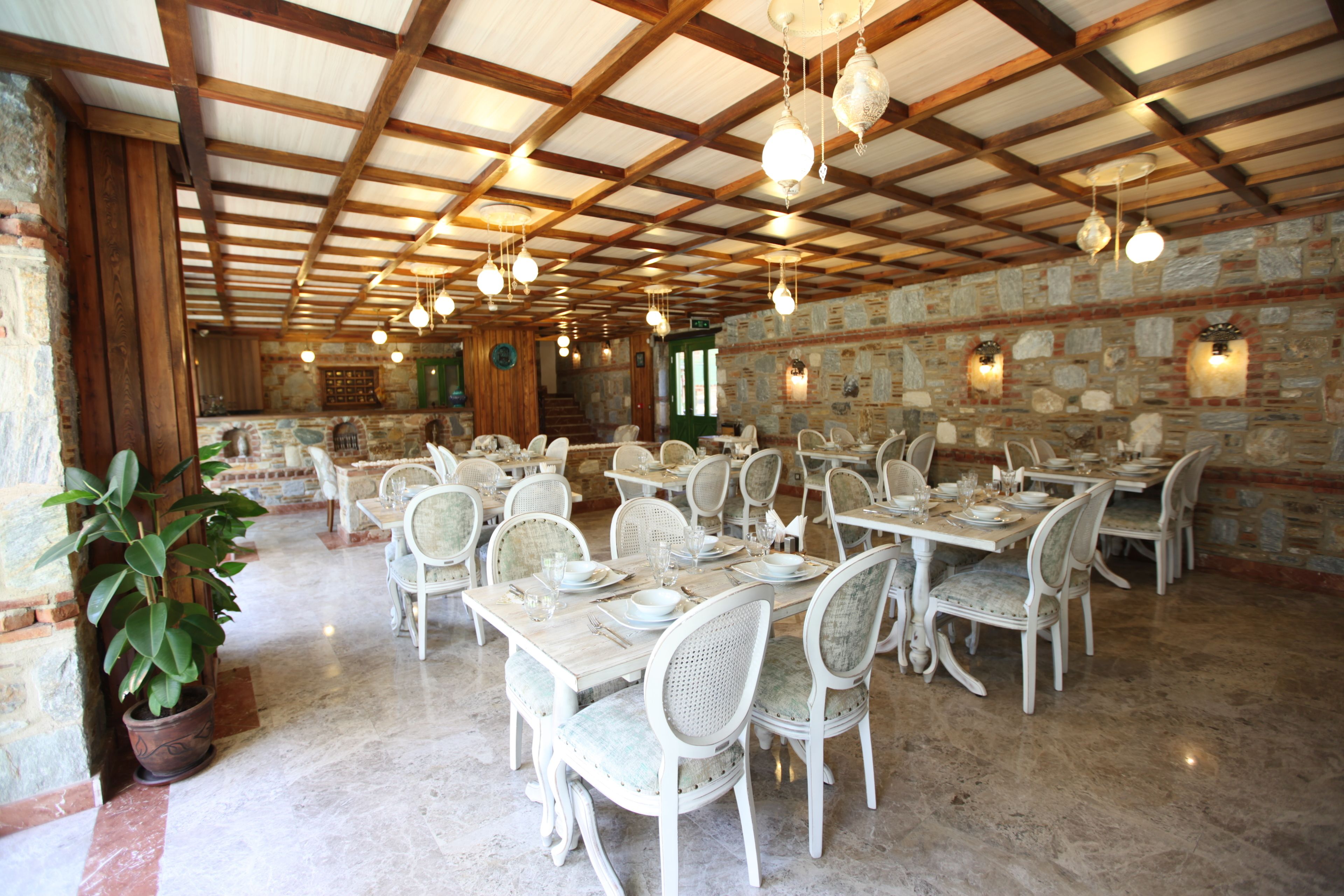 Un comedor amplio con varias mesas y sillas, paredes de piedra y lámparas colgantes.