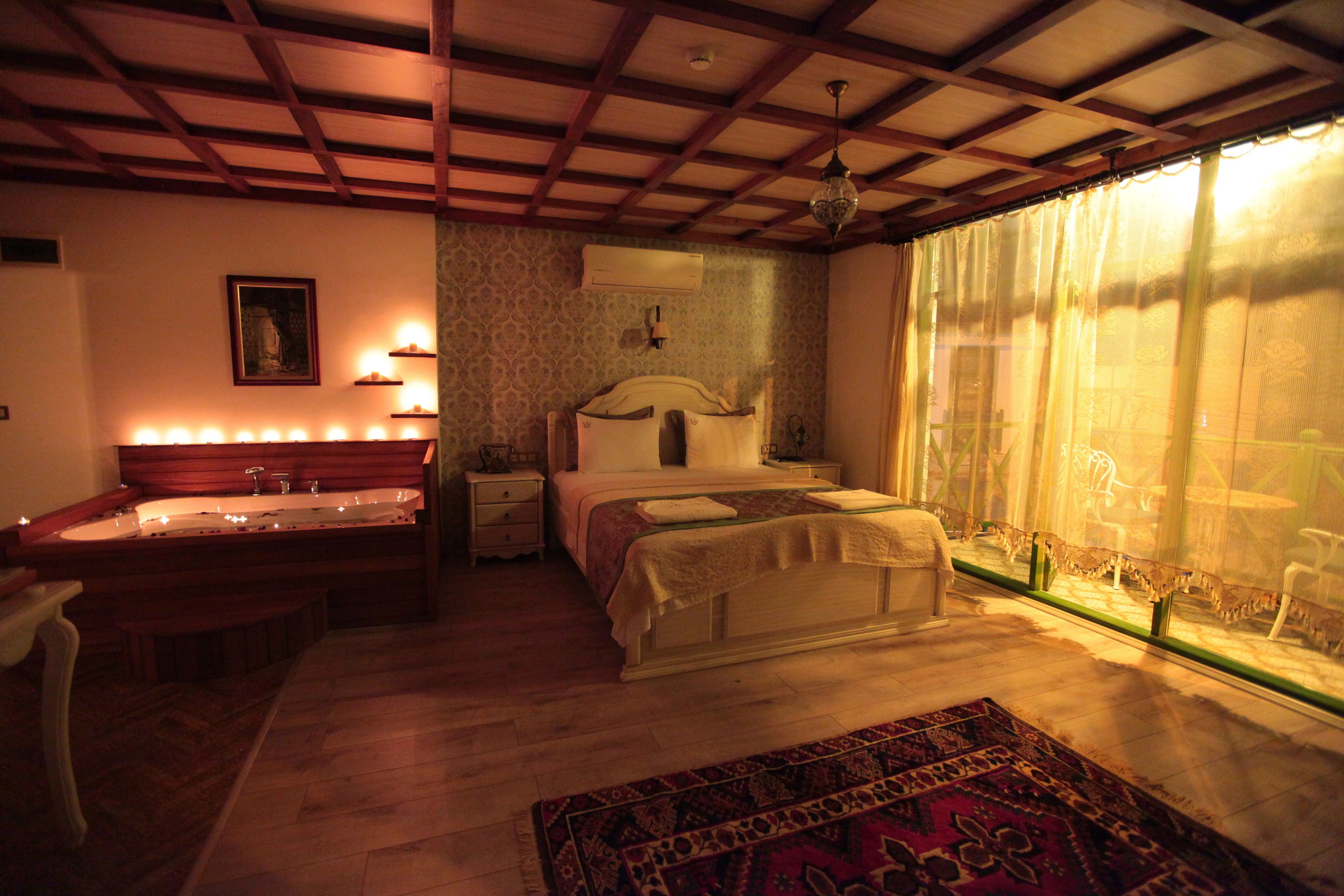 A bedroom with a large bed, a bedside table, a nightstand, a vanity with a mirror, and a window with sheer curtains.