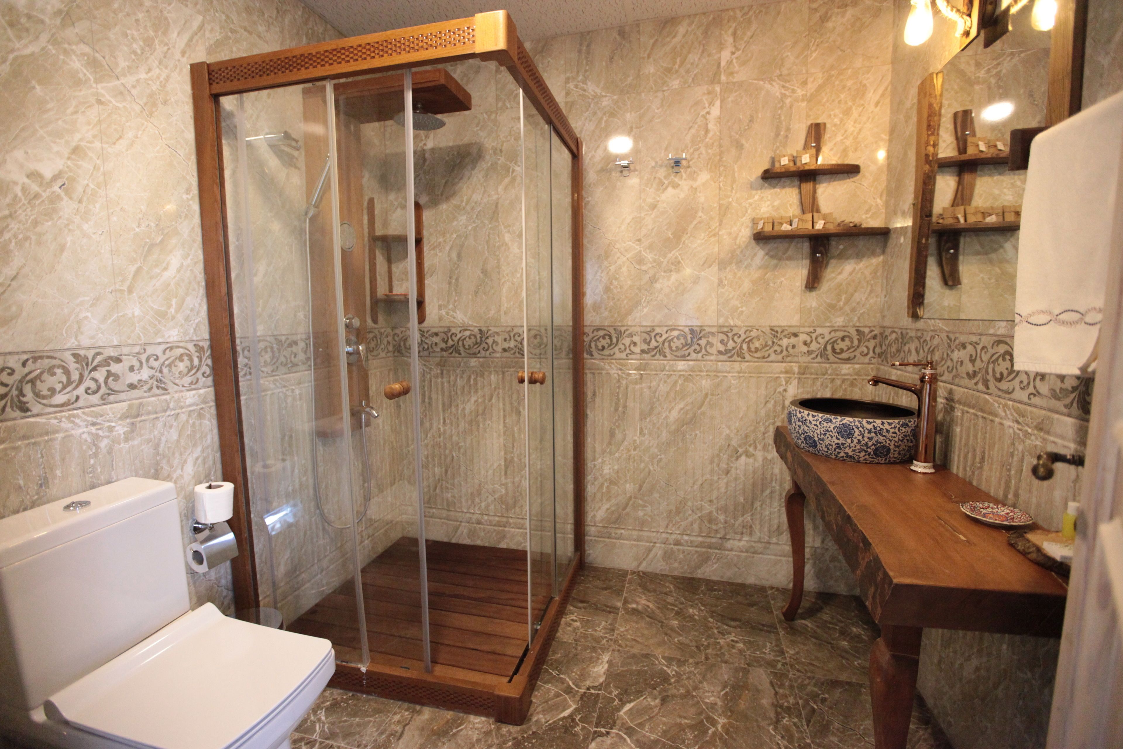 A bathroom with a glass-enclosed shower, a wooden vanity, and a marble-tiled floor.