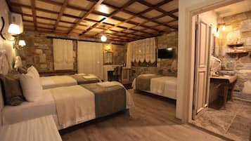 A rustic room with two beds, wooden floors, stone walls, a stone fireplace, and a television.