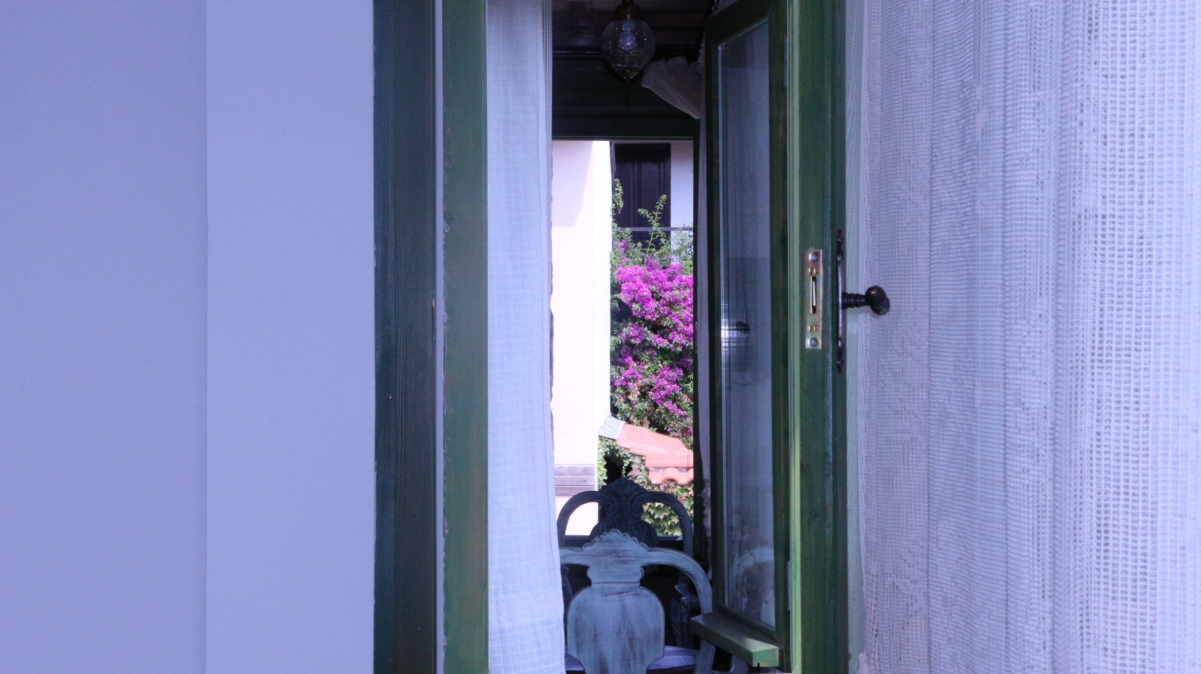 Una puerta que da a un balcón con vistas a flores moradas y una silla.