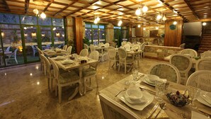 Un restaurante con varias mesas y sillas, ventanas amplias y lámparas colgantes.