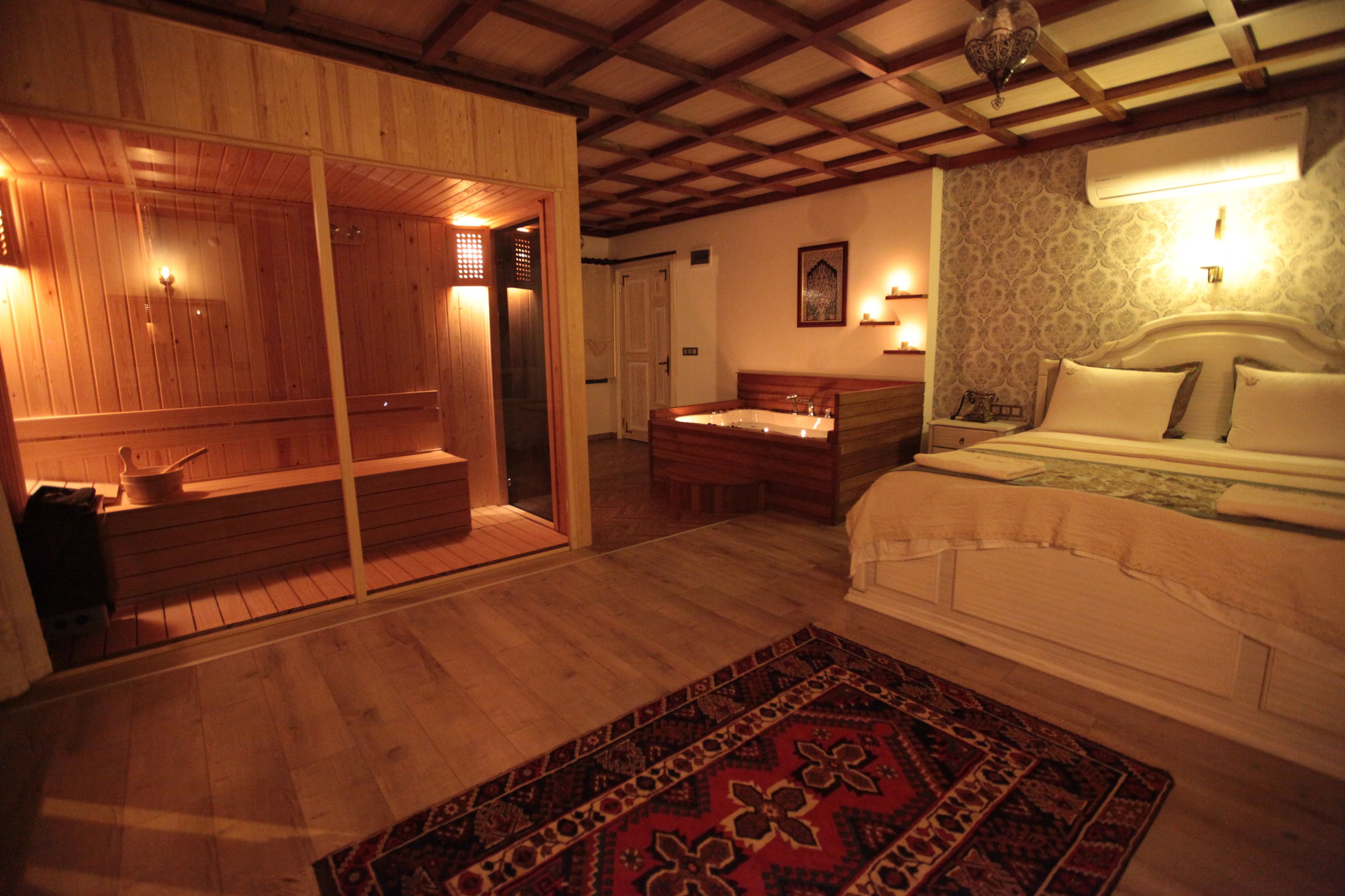 Une pièce avec un plancher en bois, un lit recouvert de draps blancs, un banc en bois et un tapis à motifs.