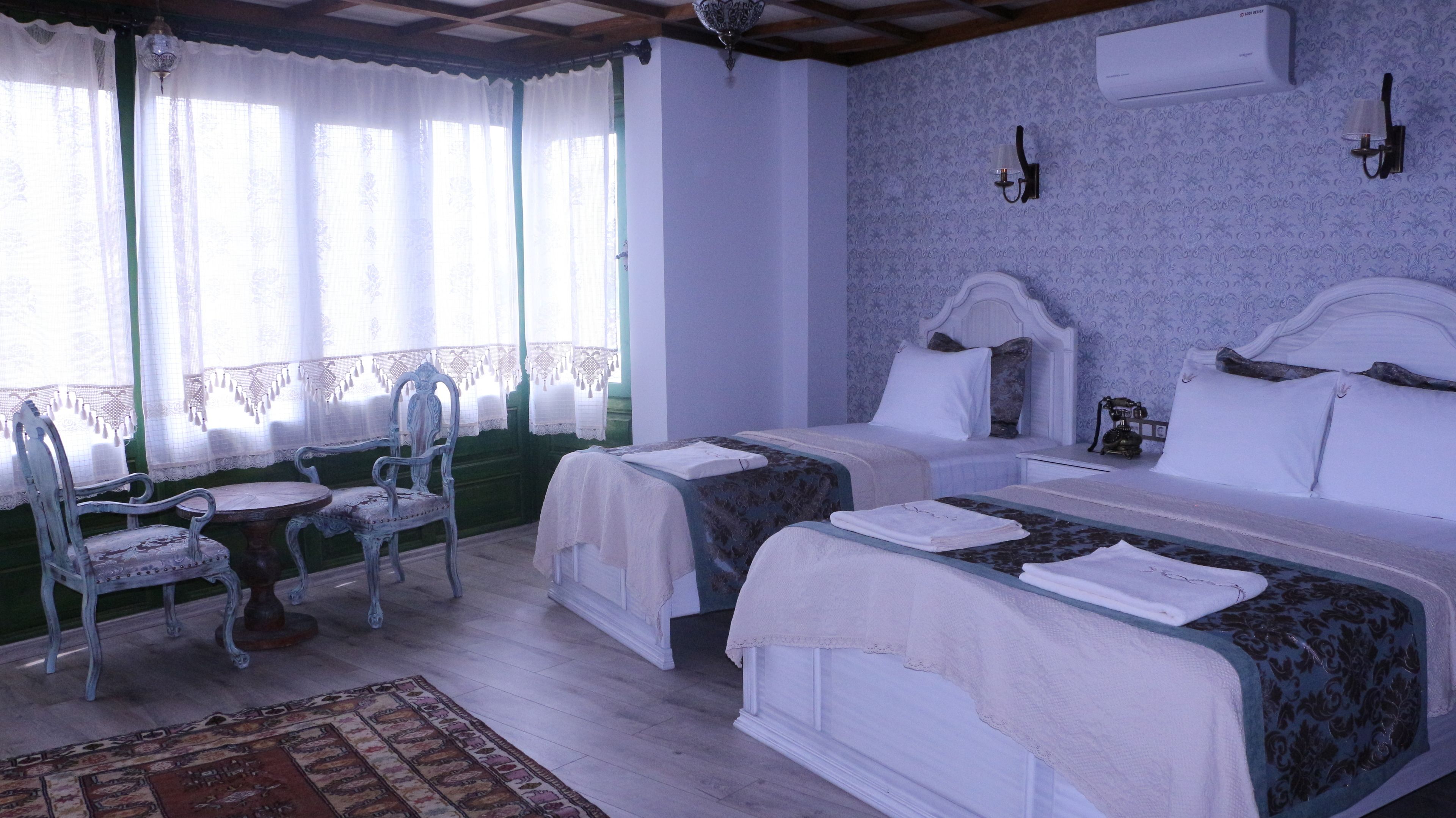 A room with two beds, a chair, a table, and a patterned rug.