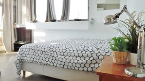 A bedroom with a bed, a desk with a lamp, a TV, and a window with curtains. - Super Central Stunning Roof 2BR Apt (Tel Aviv)