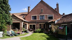 A two-story brick house with a well-maintained lawn, a patio with outdoor furniture, and a wooden fence. - Le Paddock du Val de Lys (Blessy)