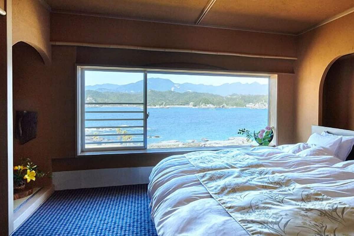 Un dormitorio con una cama grande, una ventana que ofrece vistas al mar y a las montañas, y un cuadro enmarcado en la pared.