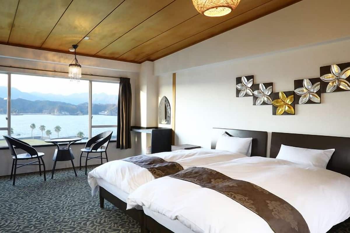 Habitación de hotel con cama, escritorio, sillas, vista al mar y decoración en la pared.
