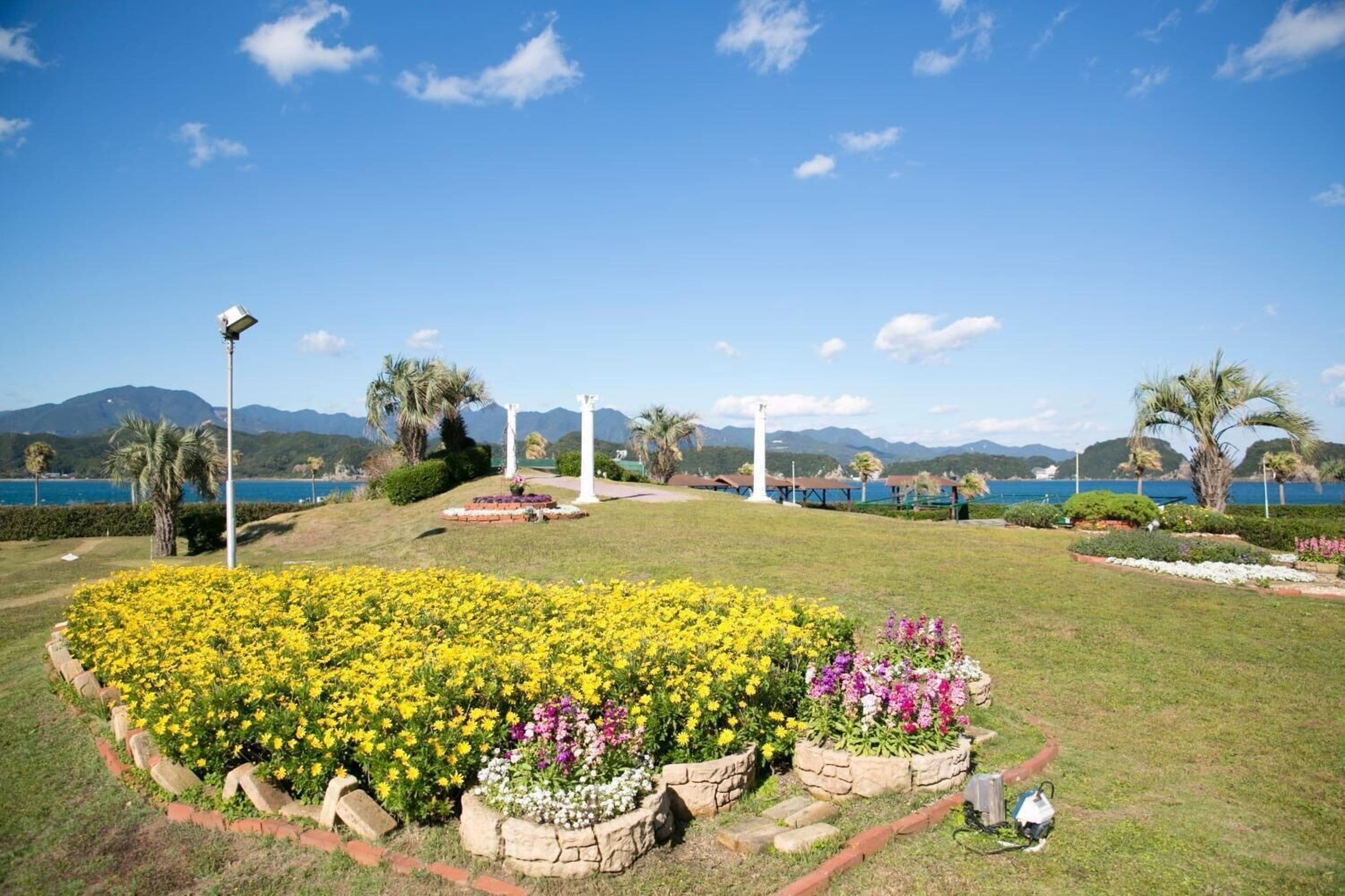 A landscaped garden with flower beds, a pathway, and a view of the sea and mountains.
