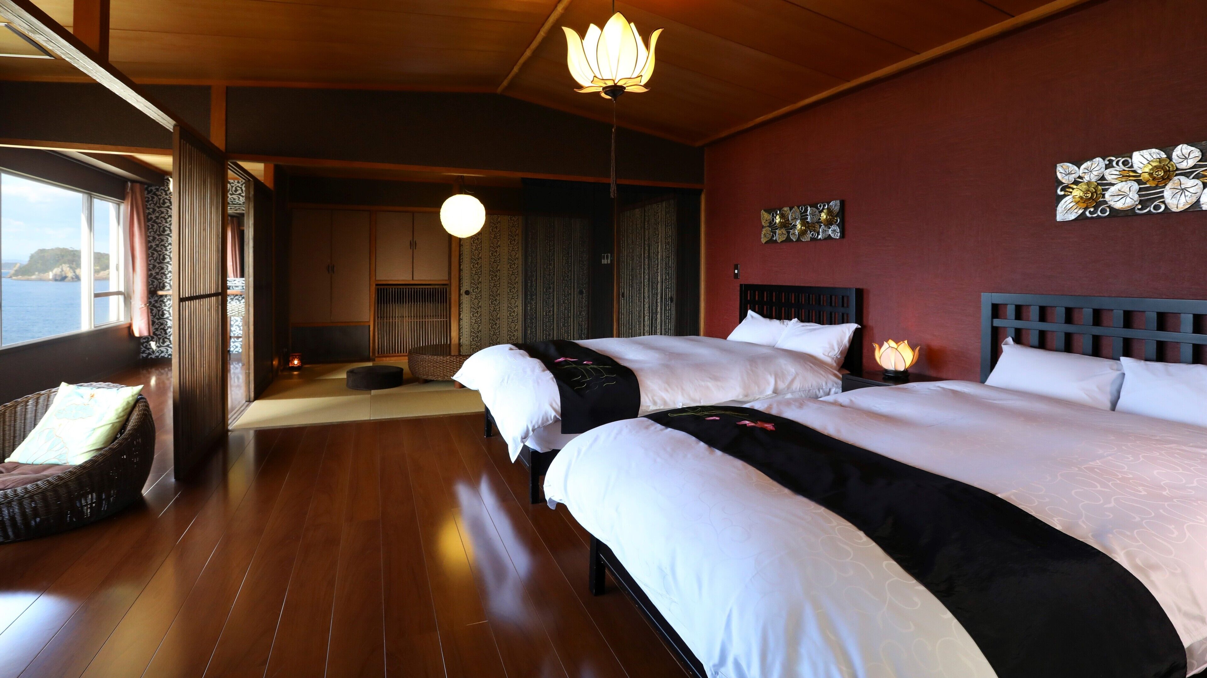 Habitación de hotel con dos camas, vista al mar, una puerta corredera tradicional japonesa y una lámpara colgante.