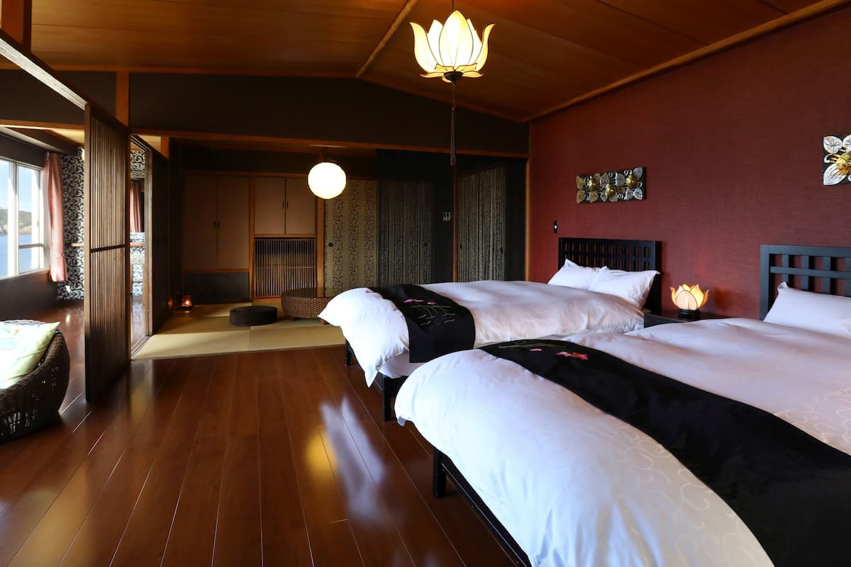 Habitación de hotel con dos camas, vista al mar, una puerta corredera tradicional japonesa y una lámpara colgante.