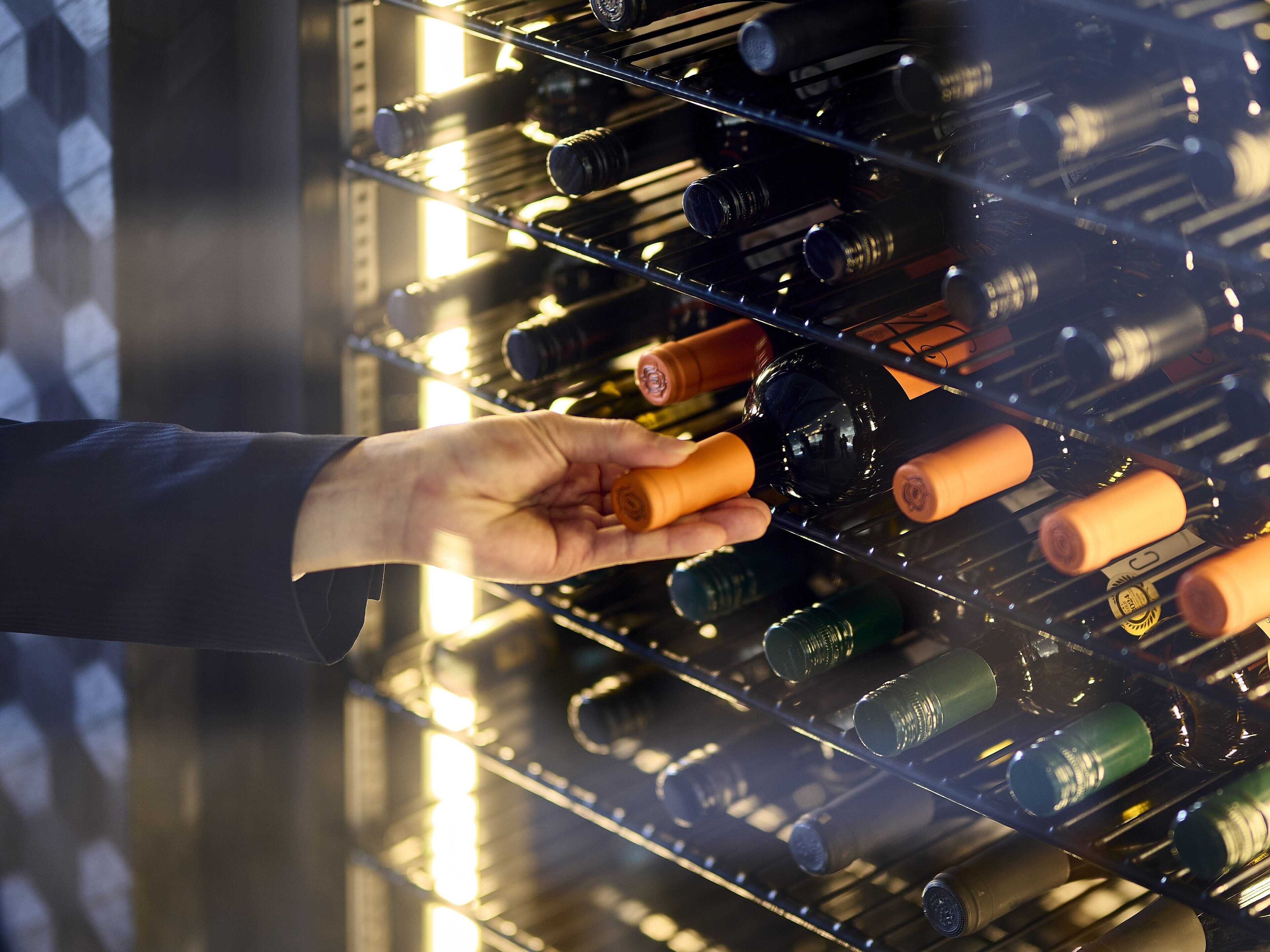 Een hand selecteert een fles uit een wijnrek in een goed verlichte opbergruimte.