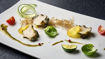 Un plato rectangular blanco con diversos alimentos, incluyendo rodajas de pepino, tomate y una verdura de hoja, sobre una superficie oscura y texturizada.