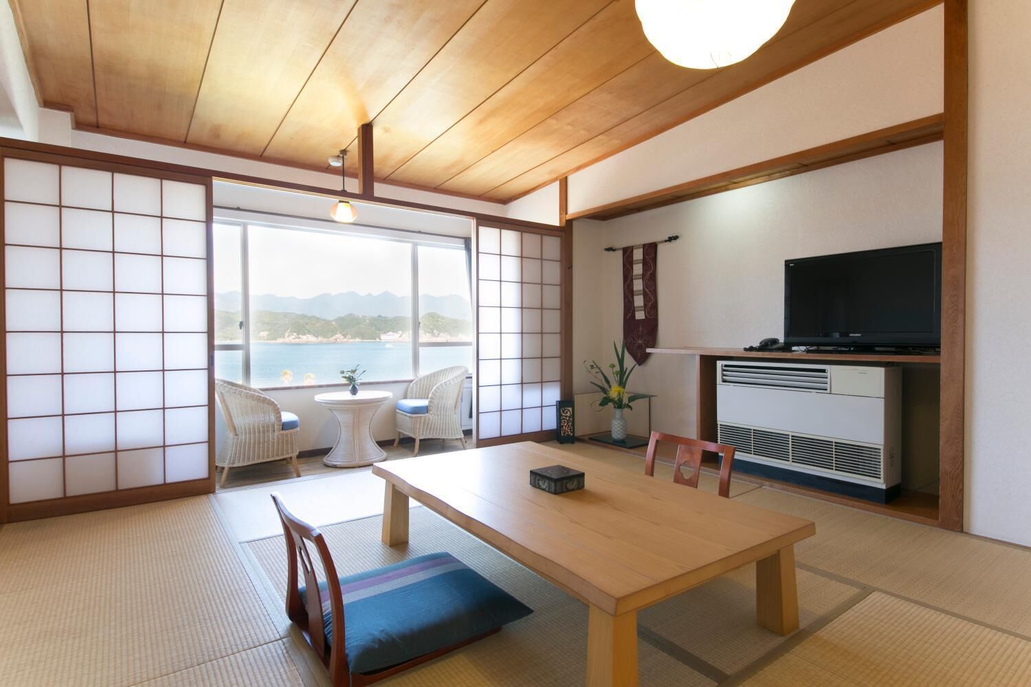 A traditional Japanese room with tatami flooring, a low table, and a TV on a wooden stand.
