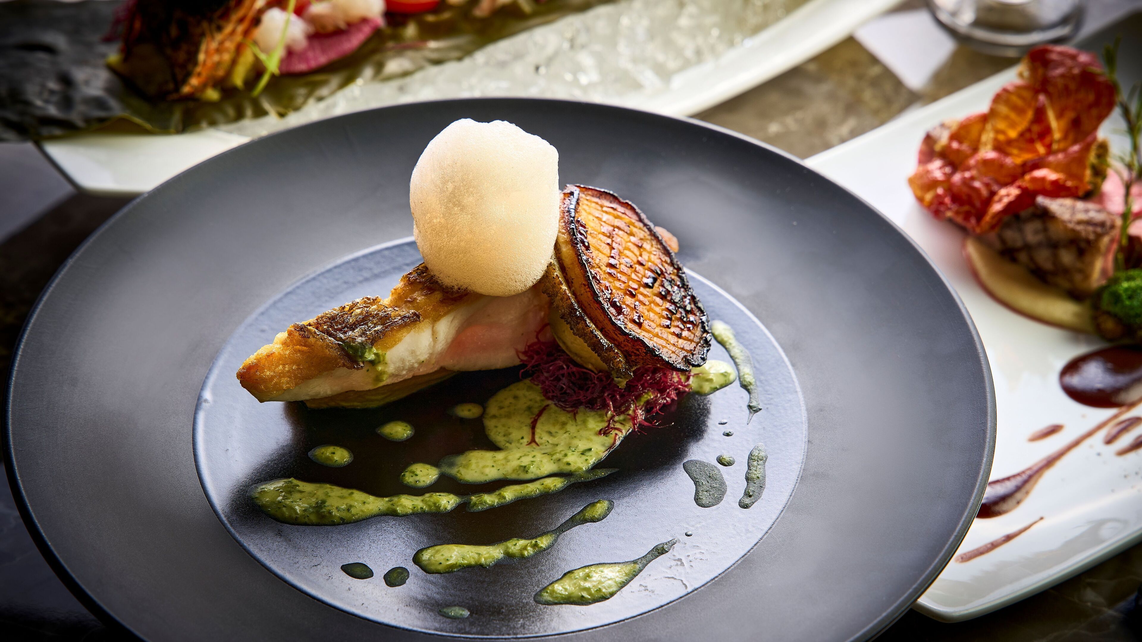 Un plato con un trozo de pescado a la parrilla, una bola de helado y salsa verde.