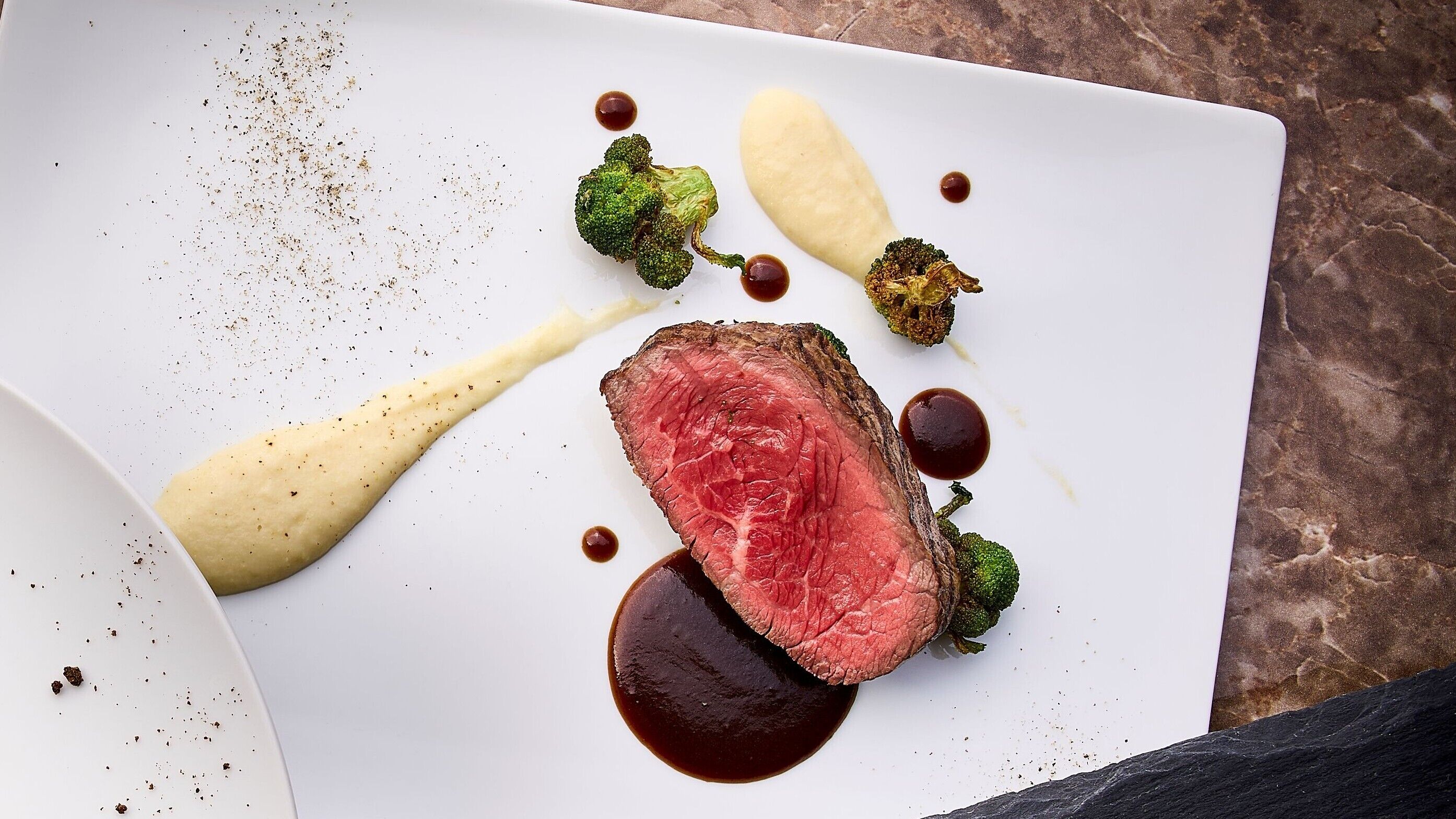 Een wit bord met steak, broccoli en sausjes.