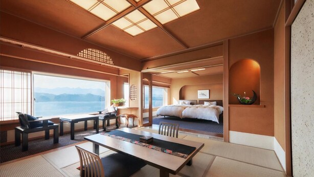 Una habitación tradicional japonesa con suelo de tatami, una mesa baja con cojines, una cama con vistas al mar y un ventanal grande.