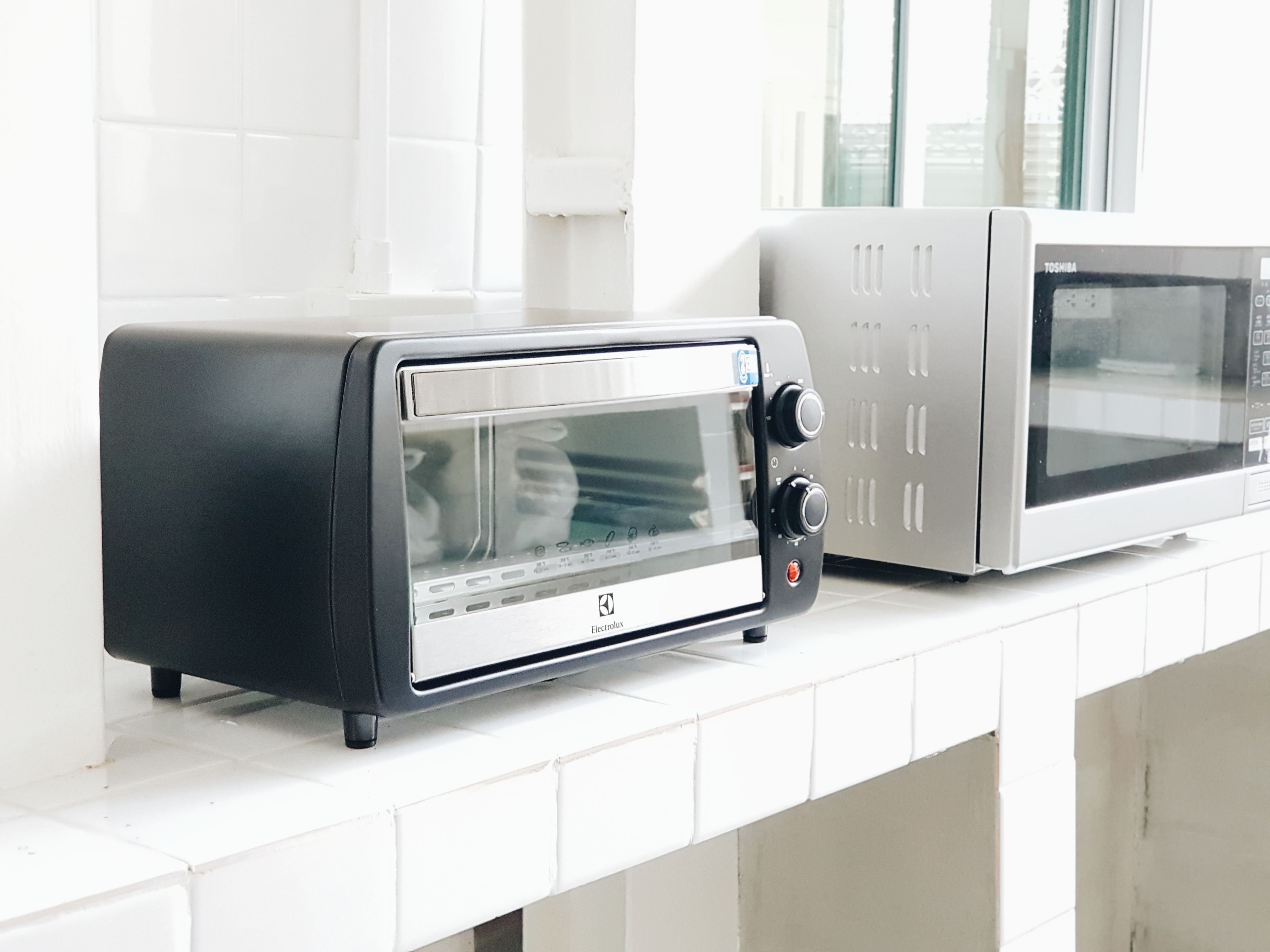 A kitchen with a black toaster and a silver microwave on a white countertop.