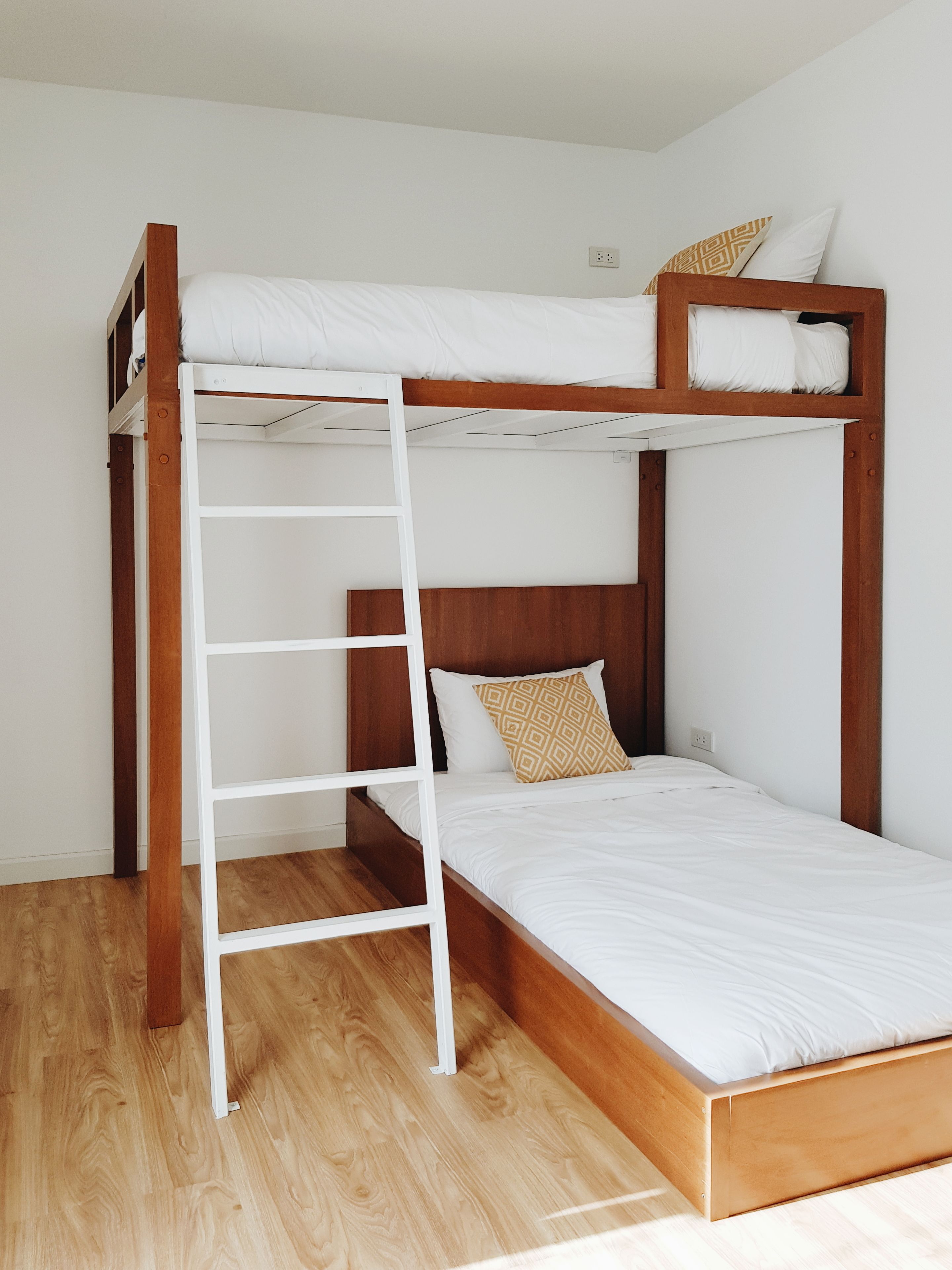 Una cama litera con escalera blanca, cabecera de madera y ropa de cama blanca.