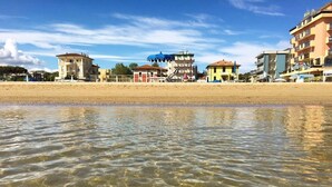 A beachfront hotel with clear waters, a sandy beach, and buildings with balconies. - Hotel Alsen (Rimini)