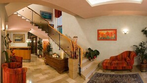 A spacious lobby with a grand staircase, a reception desk, and a comfortable seating area with potted plants. - Hotel Alsen (Rimini)