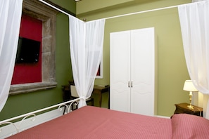Un dormitorio con cama, armario, mesita de noche, lámpara y ventana con cortinas.