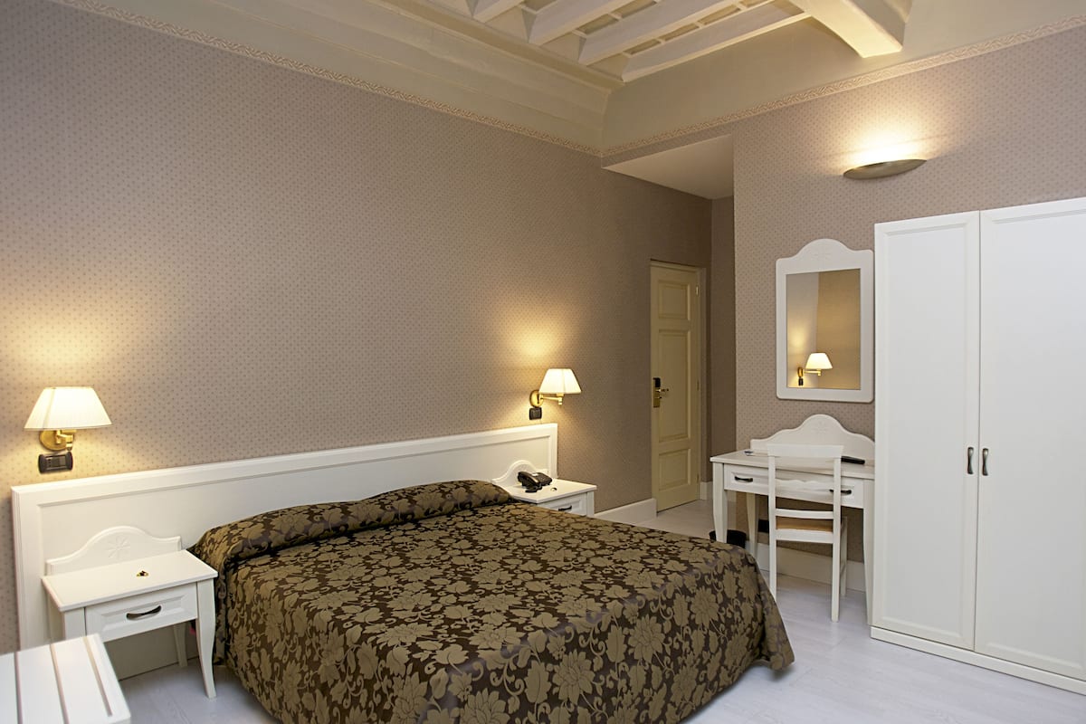 Una habitación de hotel con una cama grande, un escritorio, una silla, un armario y dos lámparas de noche.