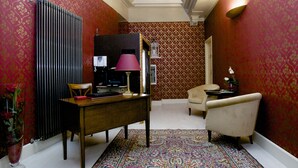 A room with a wooden desk, a chair, a patterned rug, and a radiator. - Palazzo Riario (Viterbo)