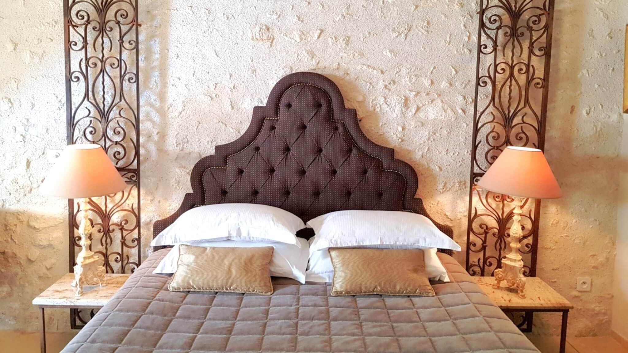 Uma cama com cabeceira estofada, duas luminárias de cabeceira e uma parede texturizada.