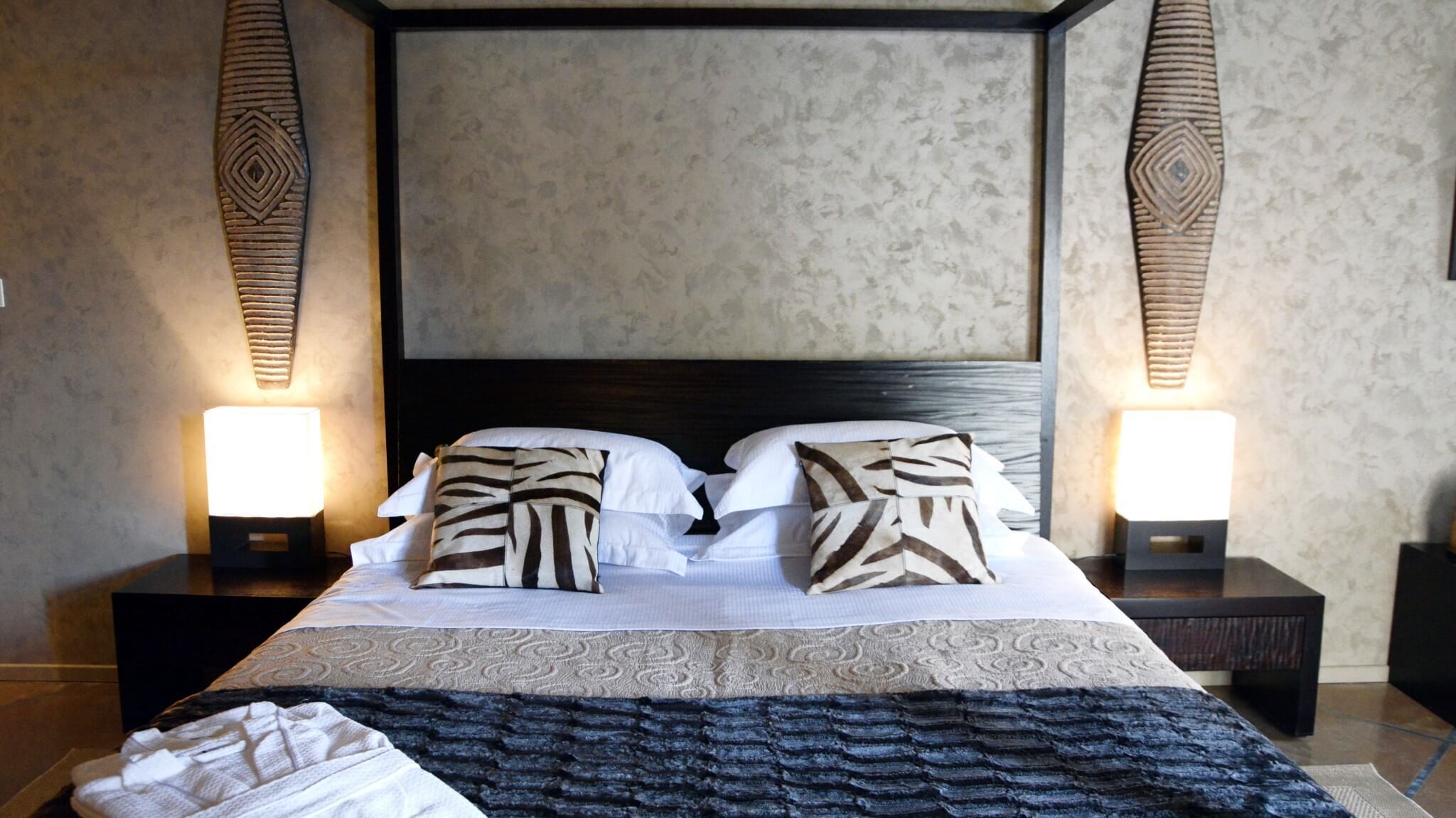 Un lit à baldaquin avec des coussins à motifs, deux lampes de chevet et une tête de lit sombre.