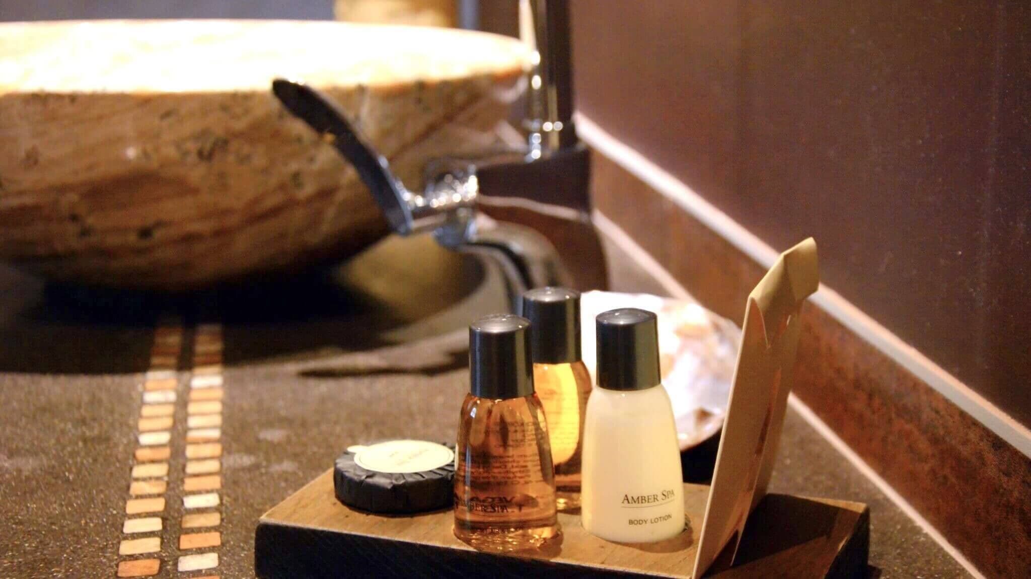 A bathroom vanity with a stone sink, a mirror, and three bottles of body lotion.