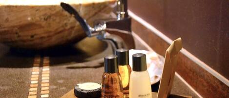 A bathroom vanity with a stone sink, a mirror, and three bottles of body lotion.
