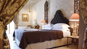 Cama bem arrumada com lençóis brancos e castanhos, cabeceira estofada escura e duas luminárias de cabeceira com abajures bege.