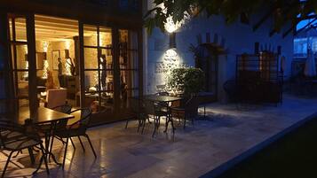 An outdoor patio area with a table and chairs, a potted plant, and a wall-mounted light fixture.
