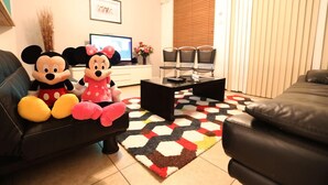 Ein Wohnzimmer mit einer schwarzen Ledersofa, zwei weichen Mickey Mouse-Spielzeugen, einem Couchtisch und einem gemusterten Teppich.