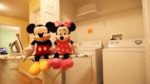 Zwei Stofftiere, eines wie Mickey Mouse und das andere wie Minnie Mouse, sitzen auf einem Wäscheständer in einem Raum mit Waschmaschine und Trockner.