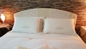 Una cama con sábanas blancas y detalles de encaje, frente a un fondo de pared de piedra.
