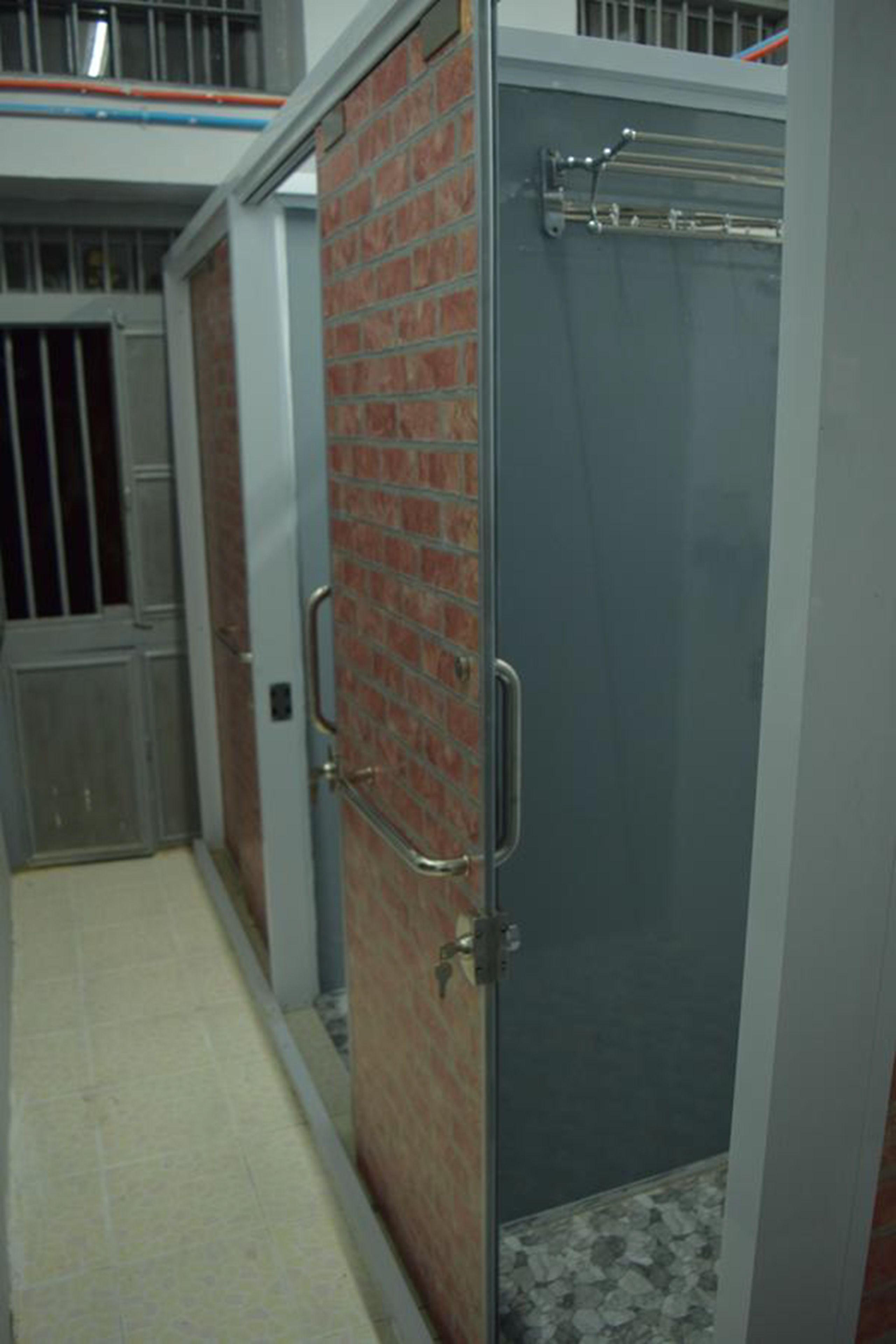 A narrow hallway with a metal door on the left and a glass shower stall on the right.