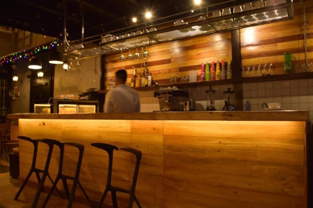 A bar area with wooden bar counter, bar stools, and hanging lights.