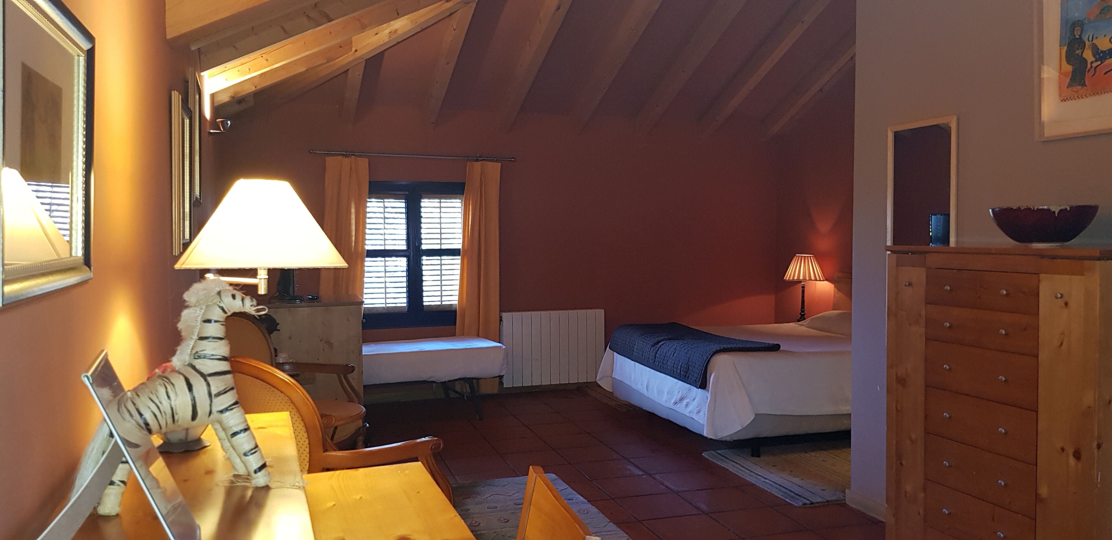 Una habitación acogedora con cama, escritorio, silla, lámpara, cómoda y ventana con cortinas.