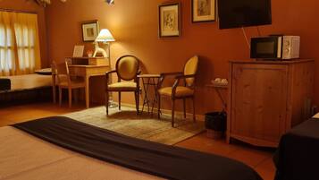 A hotel room with a bed, two chairs, a desk, a lamp, a television, and a microwave.