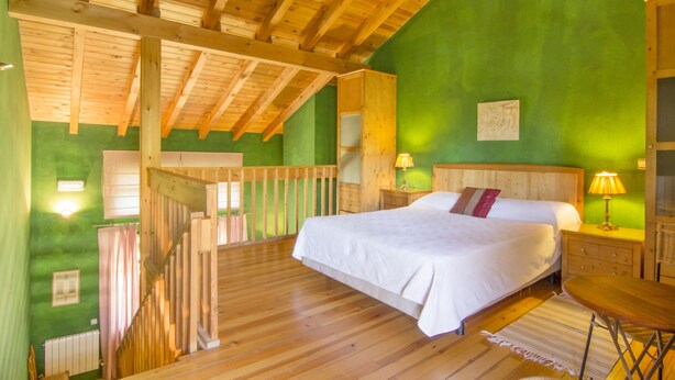 A bedroom with a wooden ceiling, a bed with white bedding, a nightstand with a lamp, and a green wall. - Hotel Sara De Ur (La Cabrera)