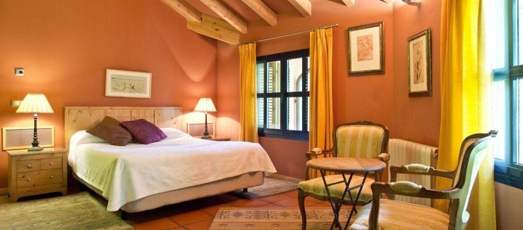 Un dormitorio con cama, lámparas de noche, una silla y un ventanal con cortinas.