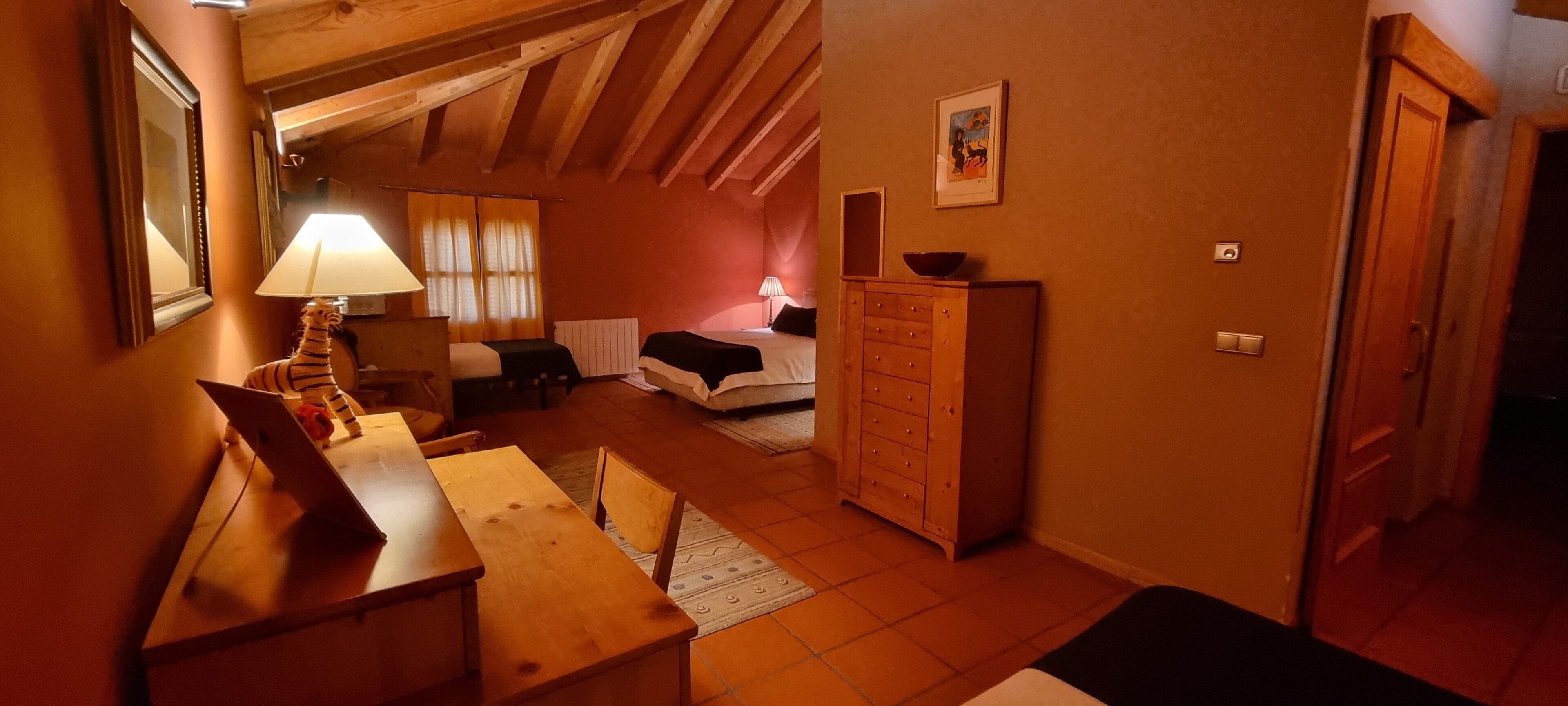 Una habitación acogedora con techo de madera, una cama, un aparador y un escritorio con lámpara.