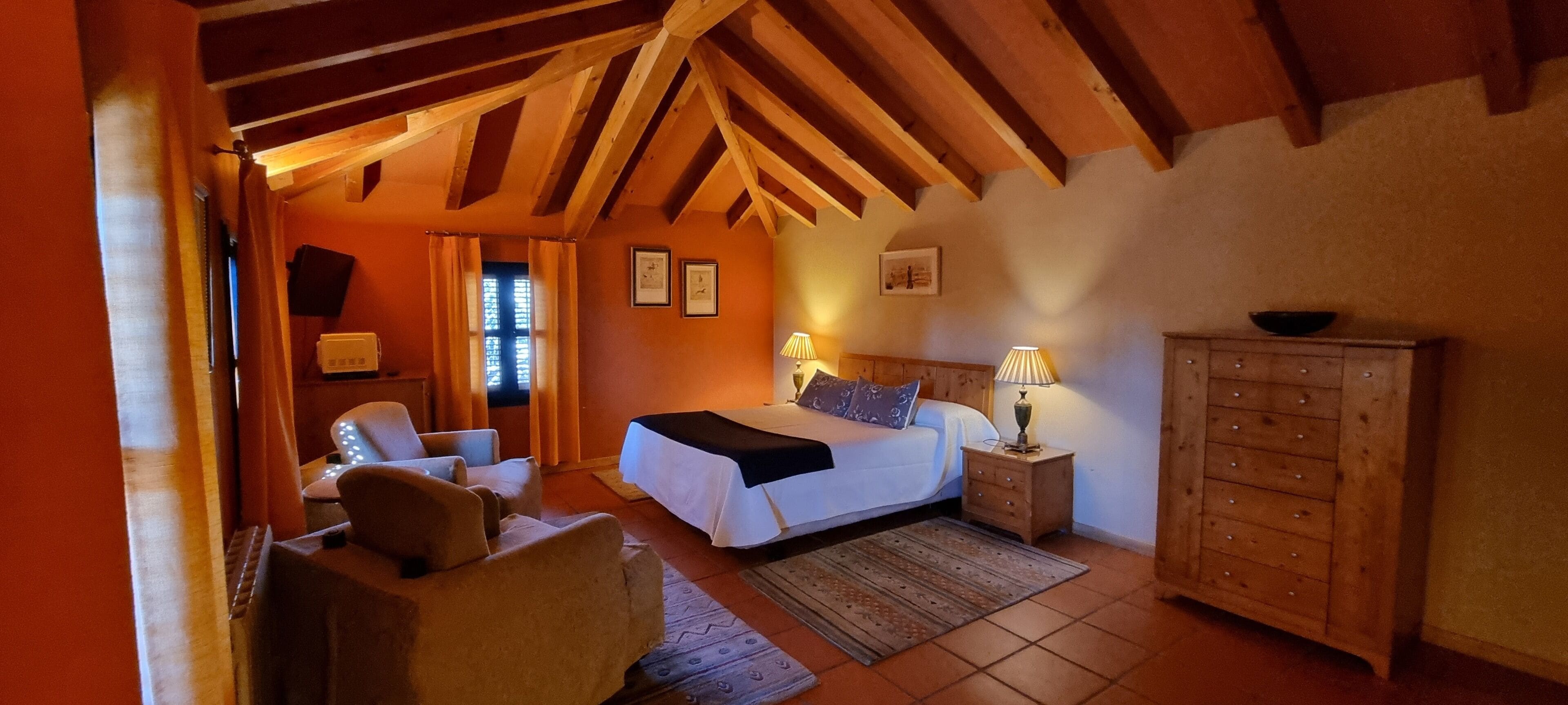 A cozy bedroom with a wooden ceiling, a bed with white bedding, two bedside lamps, a wooden dresser, and a chair.