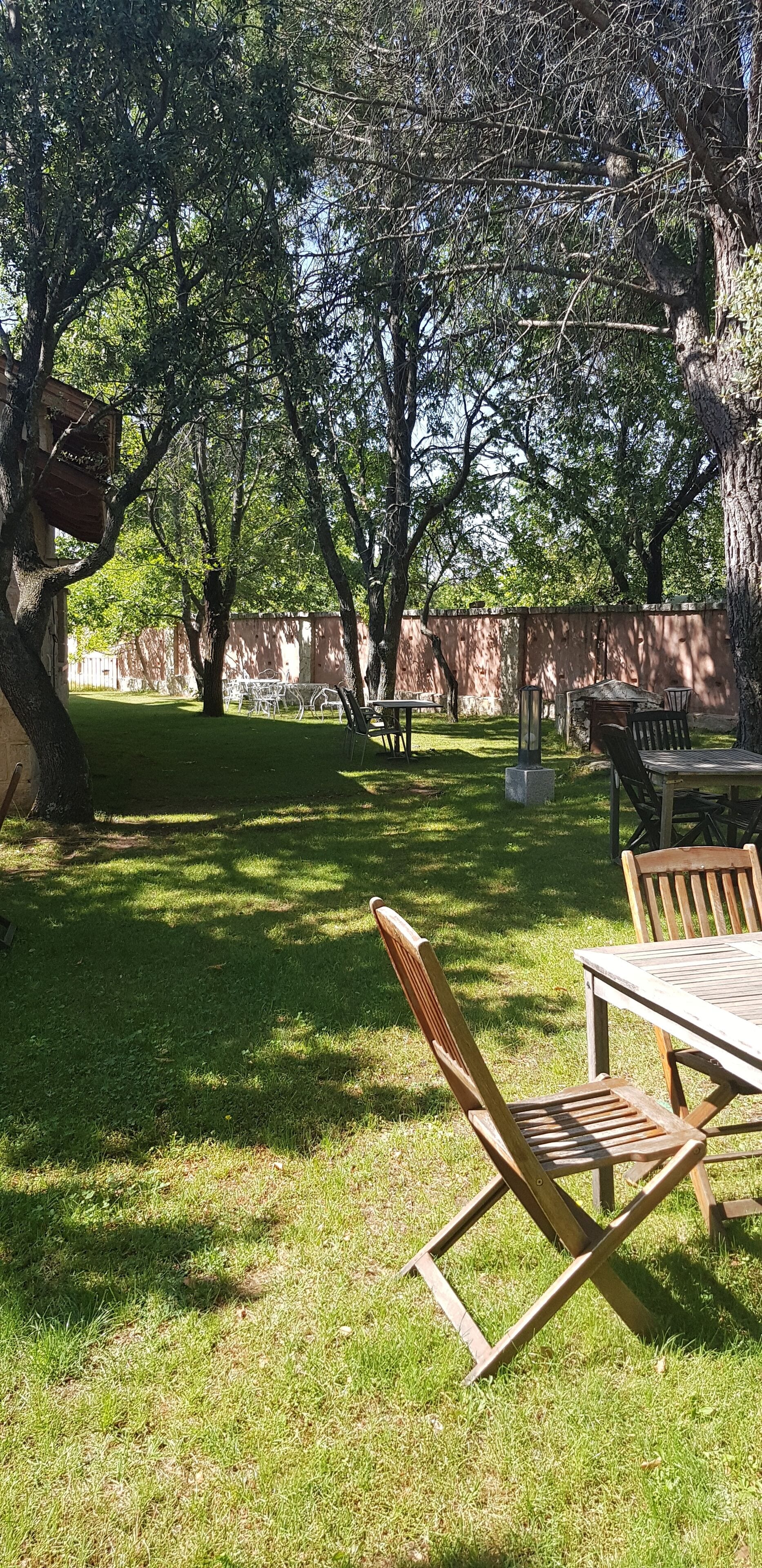 Un patio trasero con mesa y sillas de madera, rodeado de árboles y un muro de ladrillo.