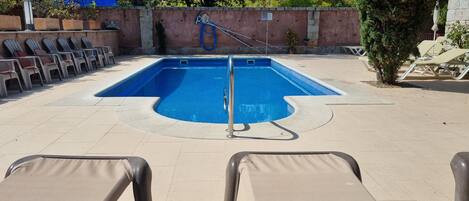 A swimming pool with lounge chairs and a hose for cleaning.