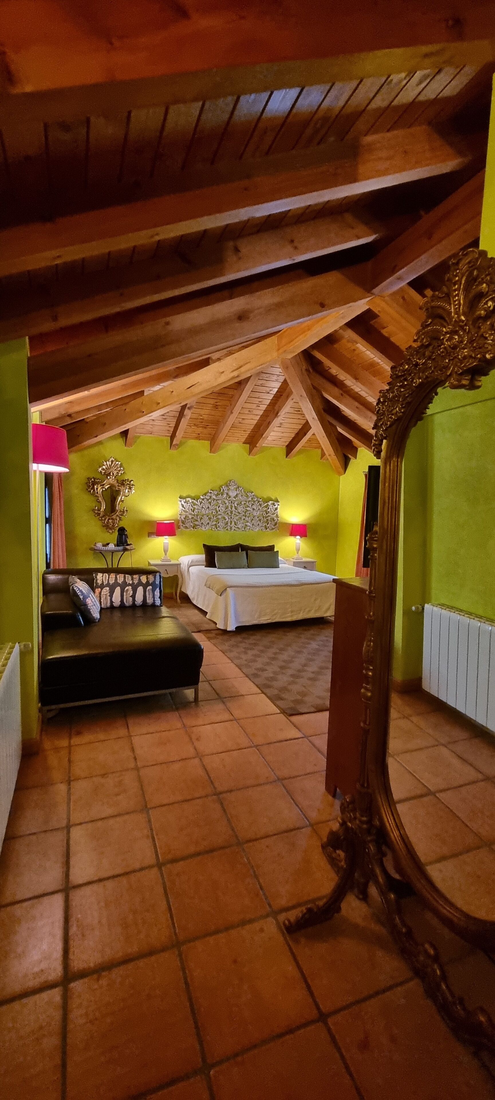 Een kamer met een schuine kap, een bed, een slaapbank en een grote spiegel.