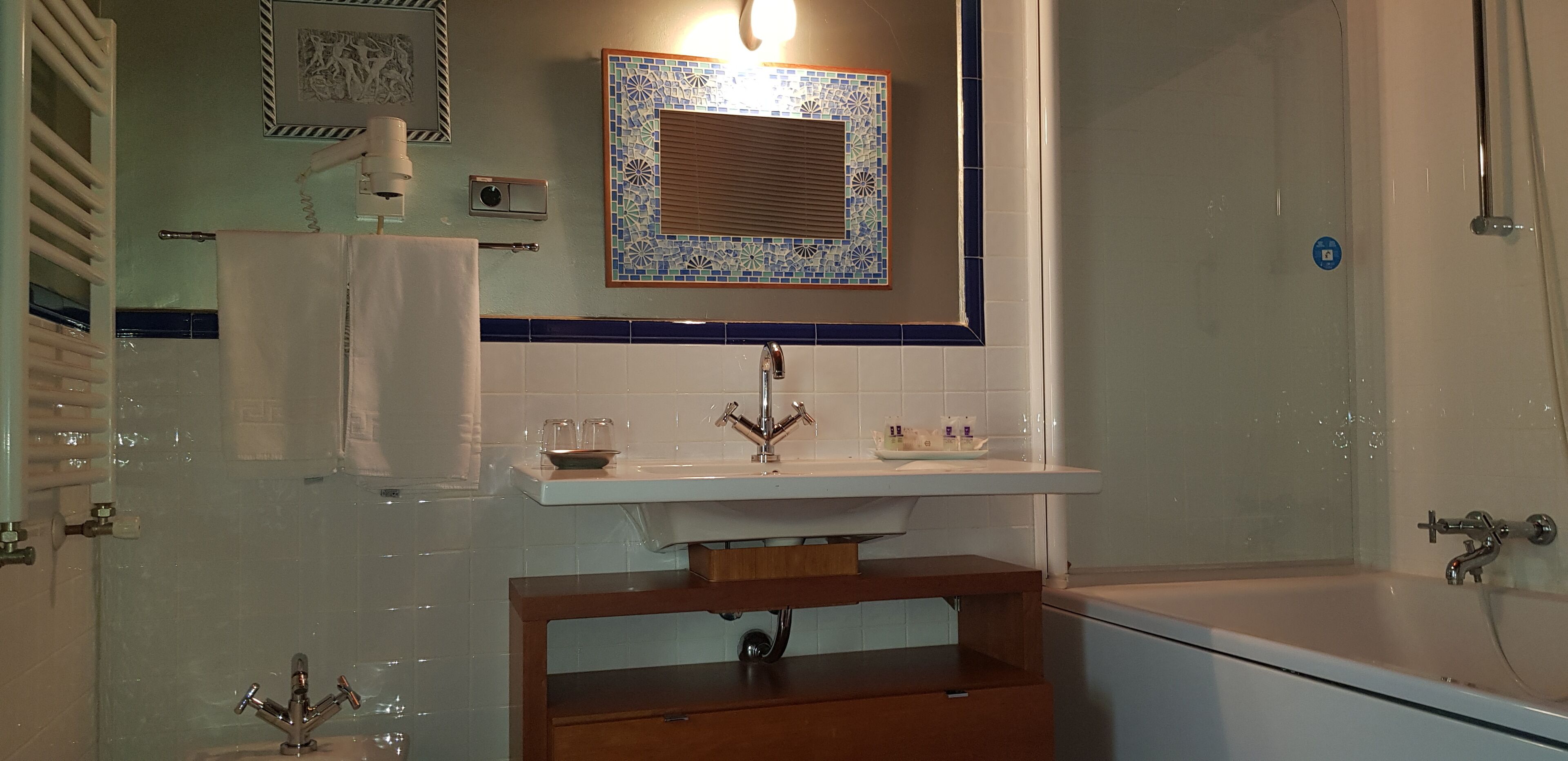 A bathroom with a white sink, a mirror with a decorative tile frame, a towel rack, and a bathtub.