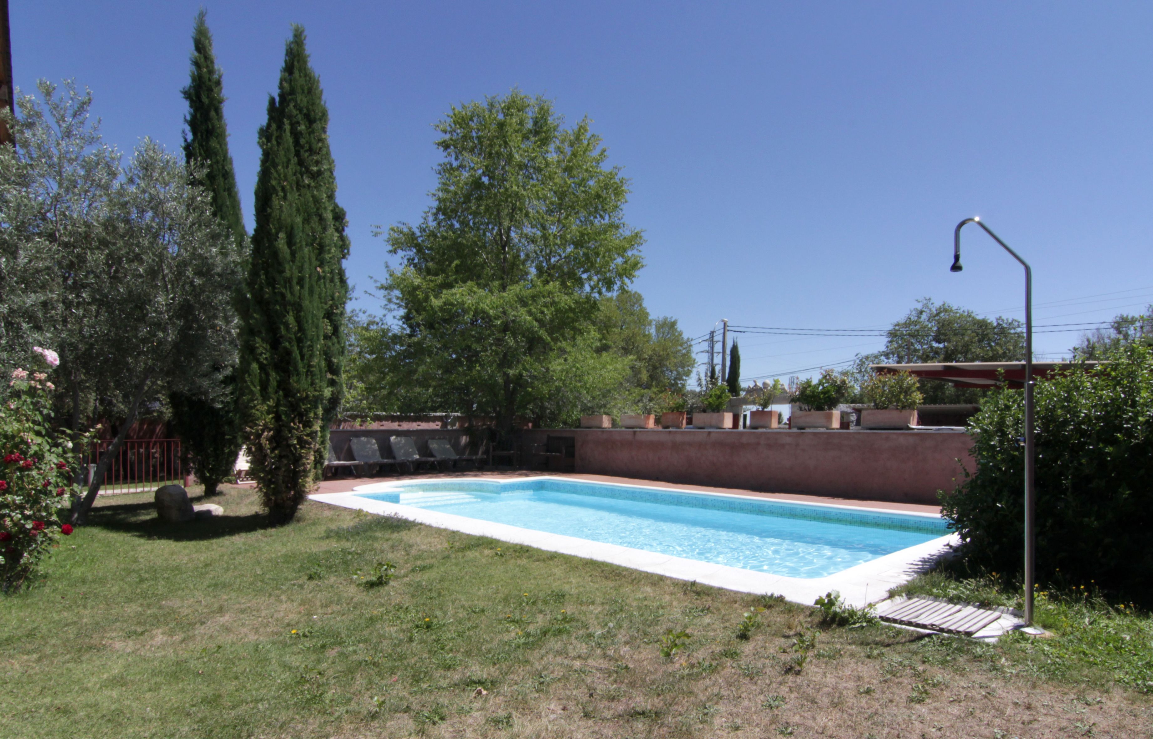 Une piscine rectangulaire bordée de carreaux, entourée d’une pelouse et d’un mur en briques.